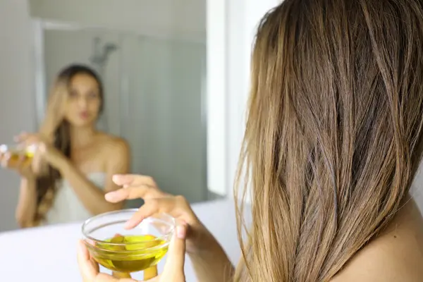 Kobieta z miseczką olejku stoi przed lustrem w łazience 